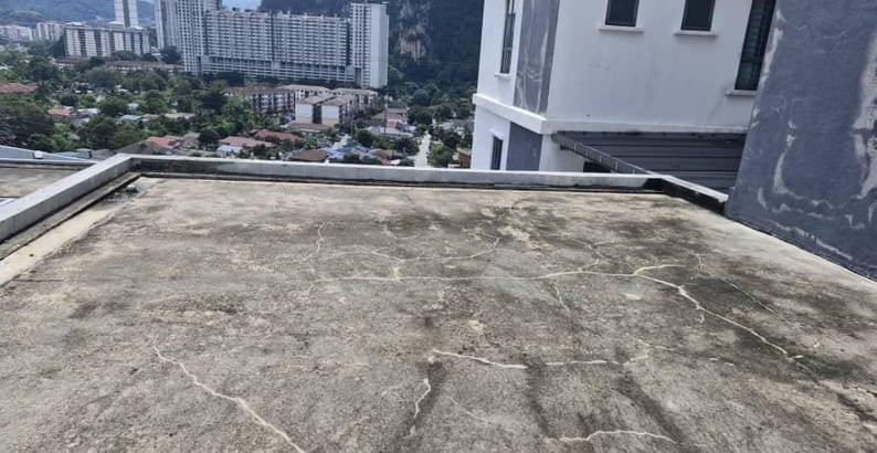 A cracked, stained rooftop slab with apartment blocks behind.