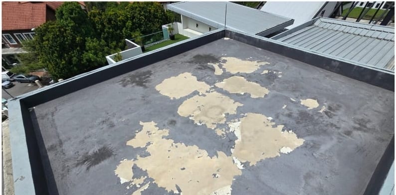 A flat roof with a grey coating peeling away in patches.